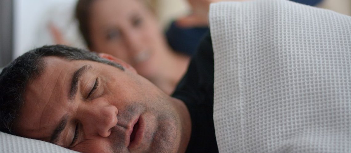 Woman (age 30) suffers from her male partner (age 40) snoring in bed. Noise concept. Real people. Copy space