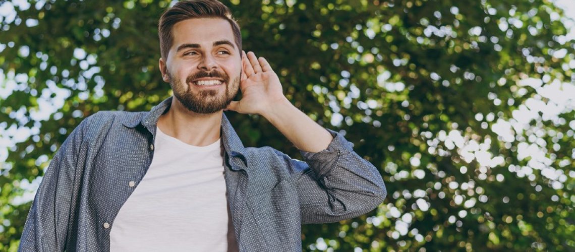 Young smiling satisfied man in blue casual shirt walk listening chirping birds rest relax in spring sunshine forest green city park go down alley outdoors on nature Urban lifestyle leisure concept.