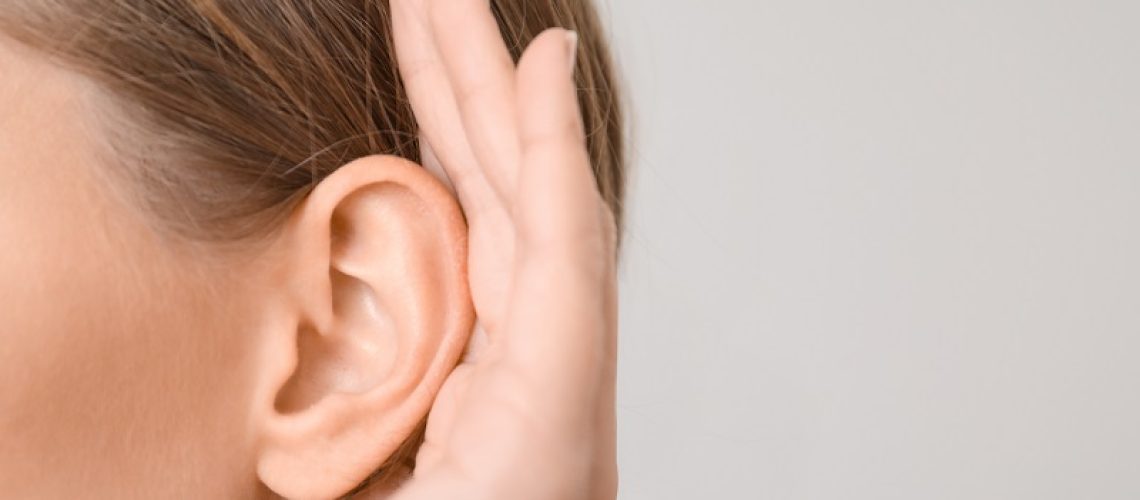 Young woman with hearing problem on light background, closeup